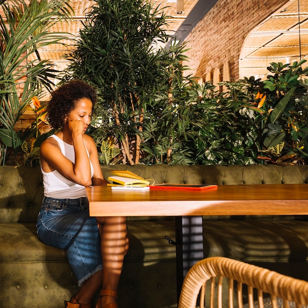 Erwogene junge Frau, die am Restauranttisch mit digitaler Tablette sitzt; Handy und Tagebuch