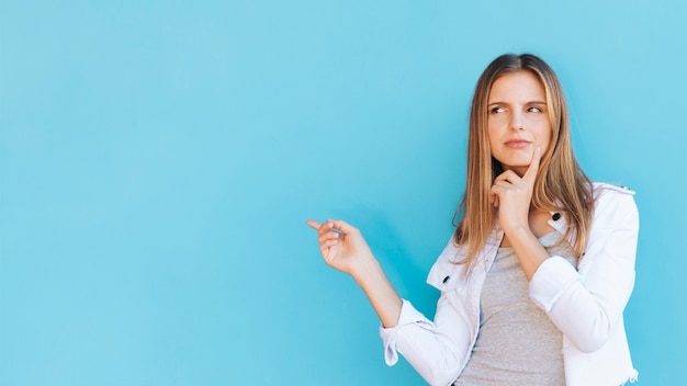 Erwogene junge Frau, die Finger gegen blauen Hintergrund zeigt