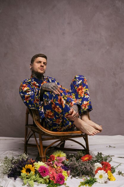 Erwogener junger Mann, der auf Stuhl mit den bunten Blumen geworfen auf Boden sitzt