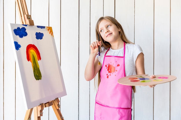 Erwogenes Mädchen, welches in der Hand die Palette und Malerpinsel stehen nahe dem Gestell hält