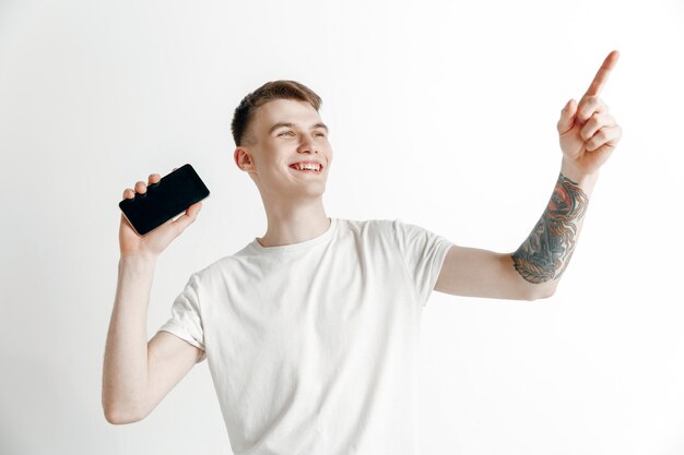 Es ist cool. Gute Nachrichten. Mach das wie ich. Junger gutaussehender Mann, der Smartphonebildschirm und Unterzeichnungs-OK-Zeichen lokalisiert auf grauem Hintergrund zeigt. Menschliche Emotionen, Gesichtsausdruck, Werbekonzept.