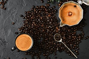 Espressokaffee mit duftendem schaum in einer tasse und in einer kanne und kaffeebohnen auf einem schwarzen tisch, flach gelegt. frühstück mit italienischem café, draufsicht der kaffeekanne auf dem tisch