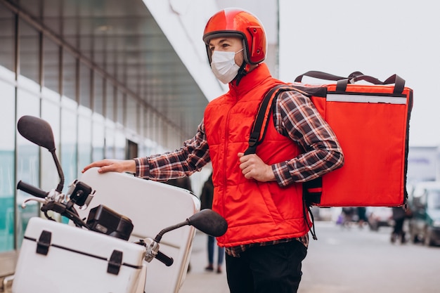 Essenslieferjunge fährt Roller mit Box mit Essen und trägt Maske