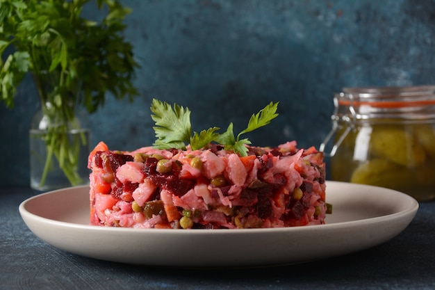Essig oder vinaigrette. traditioneller russischer roter salat mit gekochtem und eingelegtem gemüse, erbsen, rote beete, in weißer platte auf grauem hintergrund.