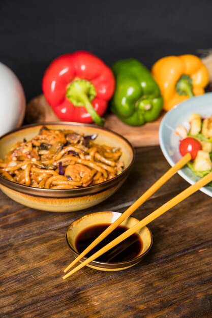 Essstäbchen mit Sojasoßenschüssel und Udon-Nudeln rollen auf Holztisch
