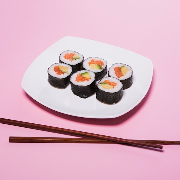 Essstäbchen nahe Platte mit Sushi auf Rosa