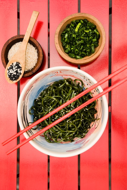 Essstäbchen über dem japanischen Chuka-Algensalat dienten mit Samen des indischen Sesams und gehackten Frühlingszwiebeln auf roter Tabelle