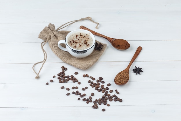 Etwas Kaffee mit gemahlenem Kaffee, Gewürzen, Kaffeebohnen in einer Tasse auf Holz- und Sackhintergrund, hohe Winkelansicht.