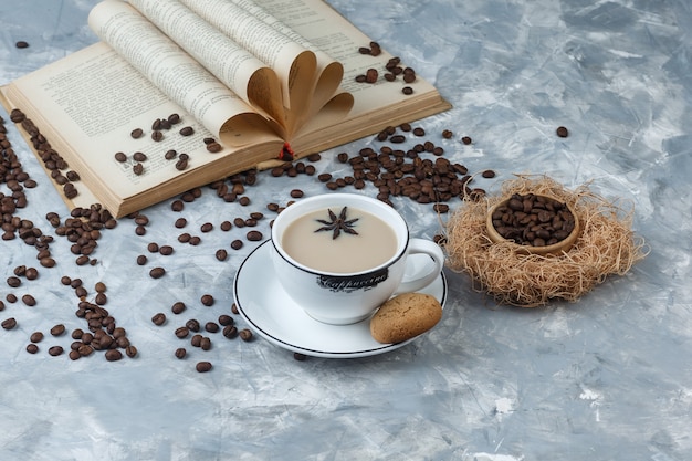 Etwas Kaffee mit Keksen, Kaffeebohnen, Buch in einer Tasse auf grauem Gipshintergrund, hohe Winkelansicht.