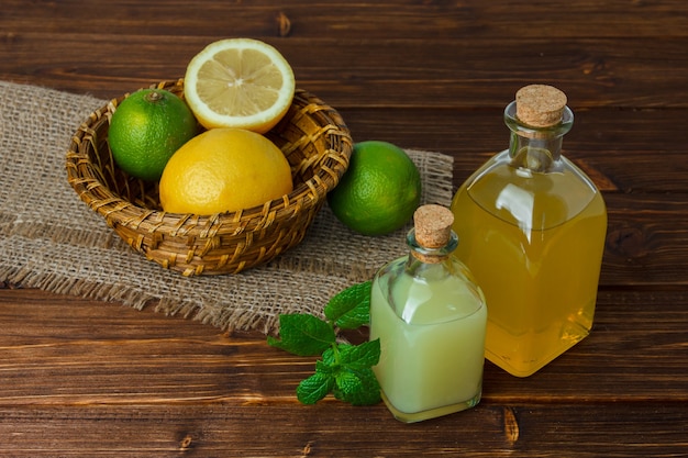 Etwas Zitrone und Saft mit der Hälfte der Zitrone auf einem Stück Sack in einem Korb auf Holzoberfläche, Blickwinkel. Platz für Text