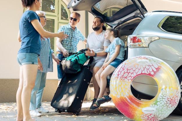 Europäische Familie lädt Taschen im Kofferraum und bereitet sich auf die Reise zum Meer vor. Kleines Kind mit Eltern und Großeltern, die mit dem Auto in den Sommerurlaub reisen.