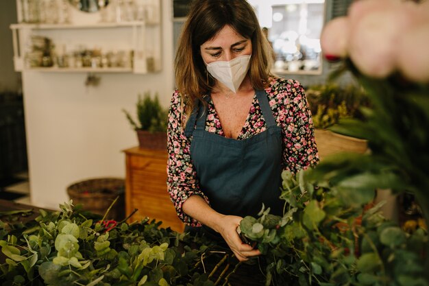 Europäische Floristin mit medizinischer Gesichtsmaske, die Blumenarrangements im Blumendesignstudio herstellt