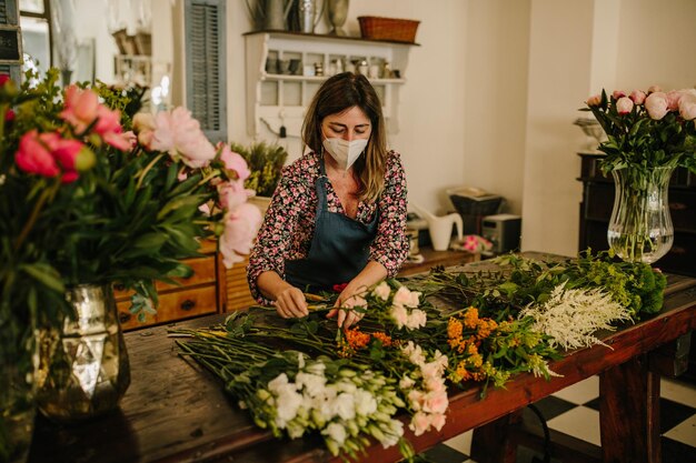 Europäische Floristin mit medizinischer Gesichtsmaske, die Blumenarrangements im Blumendesignstudio macht