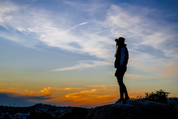 Europäische Frau mit Cowboyhut, die auf einem Felsen steht und den Sonnenuntergang beobachtet