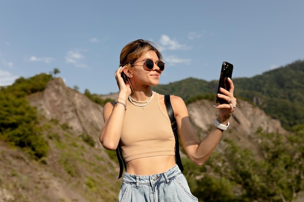 Europäische Frau mit hellem Haar in Sonnenbrille macht Foto der Natur im Sonnenlicht gegen Berge Reisekonzept Frau reist in Europa Berge