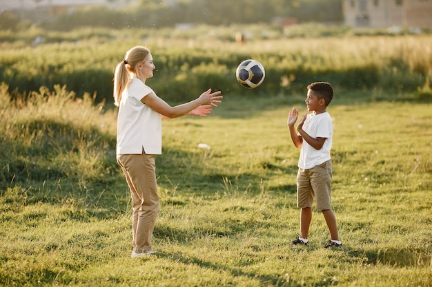 Europäische Mutter und afrikanischer Sohn. Familie in einem Sommerpark. Die Leute spielen mit dem Ball.