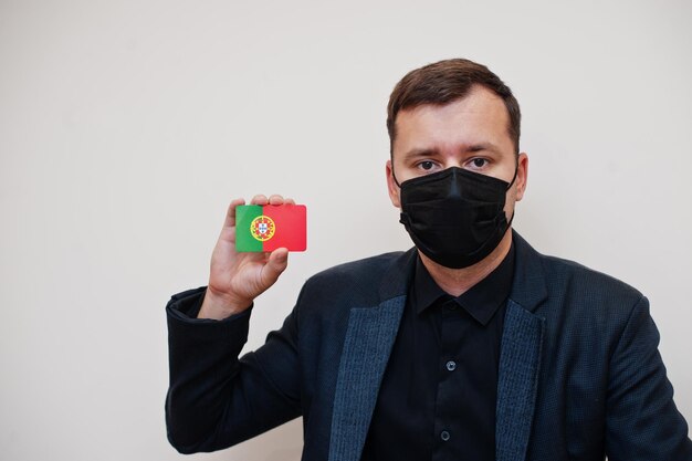 Europäischer Mann trägt schwarzes formelles und schützt Gesichtsmaske hält Portugal-Flaggenkarte isoliert auf weißem Hintergrund Europa Coronavirus Covid Länderkonzept