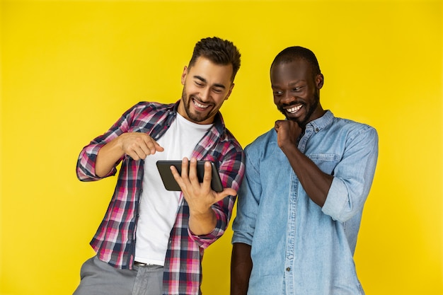 Europäischer Typ zeigt etw auf dem Tablet und er lacht zusammen mit Afroamerikaner