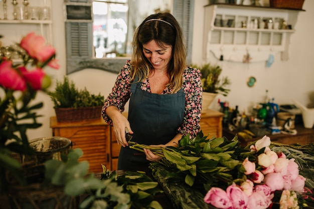 Europäischer weiblicher Florist mit einer grünen Schürze, die Blumenarrangements macht
