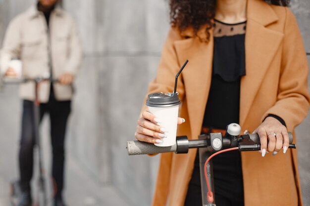 Europäisches Mädchen anindian Kerl fahren Roller und lächeln. Leute mit Kaffee.