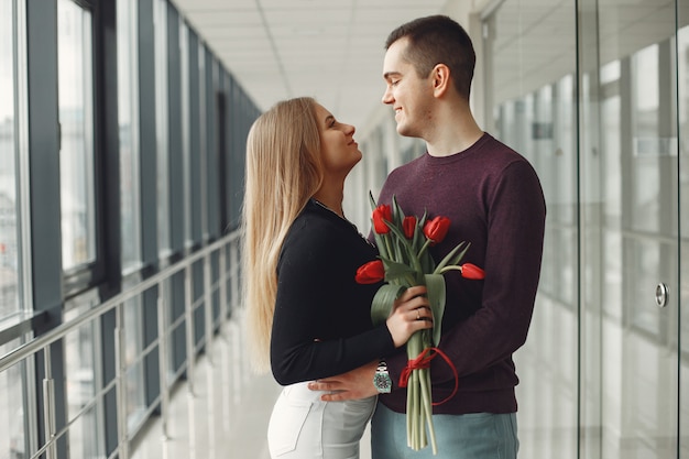 Europäisches Paar steht in einer Halle mit einem Bündel roter Tulpen