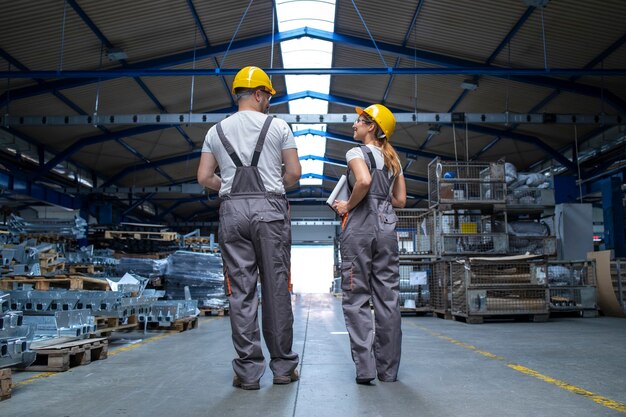 Fabrikarbeiter gehen durch große Produktionshalle und unterhalten sich