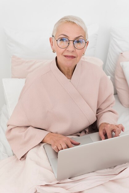 Fällige Frau im Bett, das an Laptop arbeitet