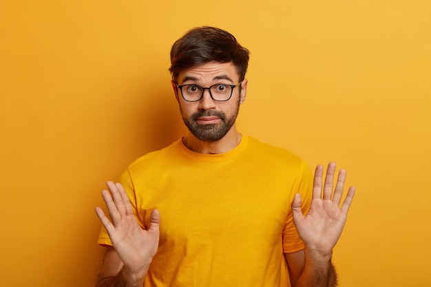 Fahrlässigkeitskonzept. Der bärtige junge Mann drückt unbeschwerte Verantwortung aus, sagt überhaupt nicht mein Problem, hebt die Handflächen, trägt eine Brille und ein lässiges T-Shirt und ist an etwas nicht beteiligt