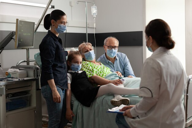 Familie, die ältere ältere Patientin besucht, während sie eine schützende Gesichtsmaske trägt