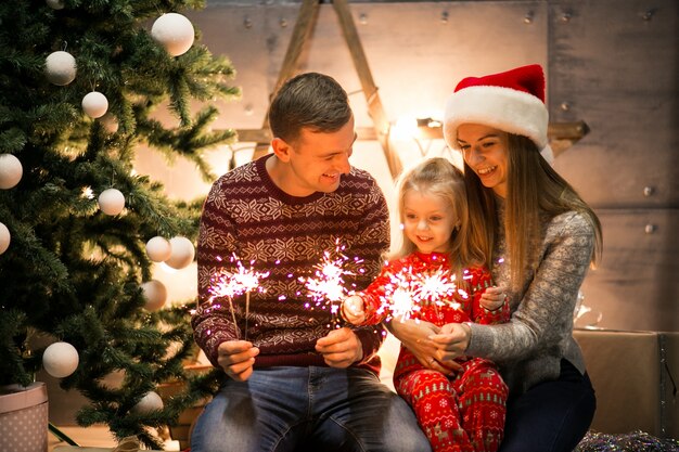 Familie, die durch den Weihnachtsbaum mit Bengal-Lichtern sitzt