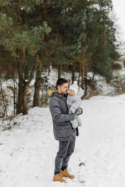 Familie, die im Schnee spazieren geht, der Spaß im Winterpark an einem hellen Tag hat, der einander umarmt und lächelt
