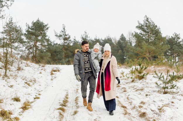 Familie, die im Schnee spazieren geht, der Spaß im Winterpark an einem hellen Tag hat, der einander umarmt und lächelt