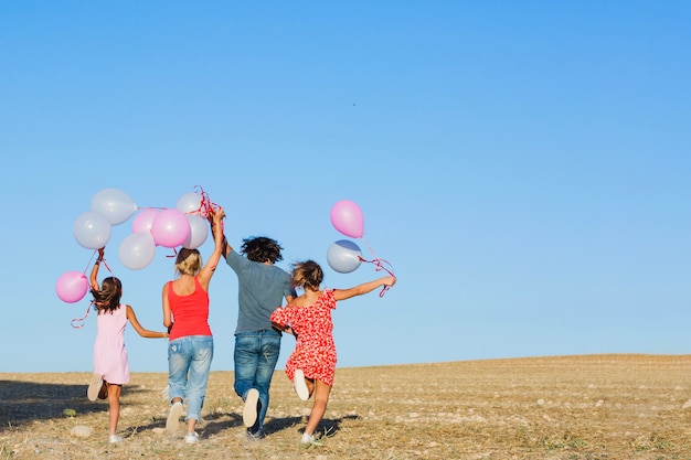 Familie, die in Feld mit Ballonen läuft