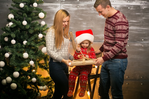 Familie durch den Weihnachtsbaum mit kleiner Tochter in einem roten Hut