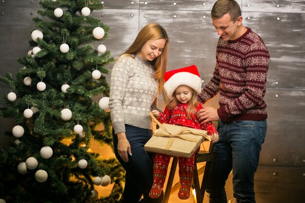 Familie durch den Weihnachtsbaum mit kleiner Tochter in einem roten Hut