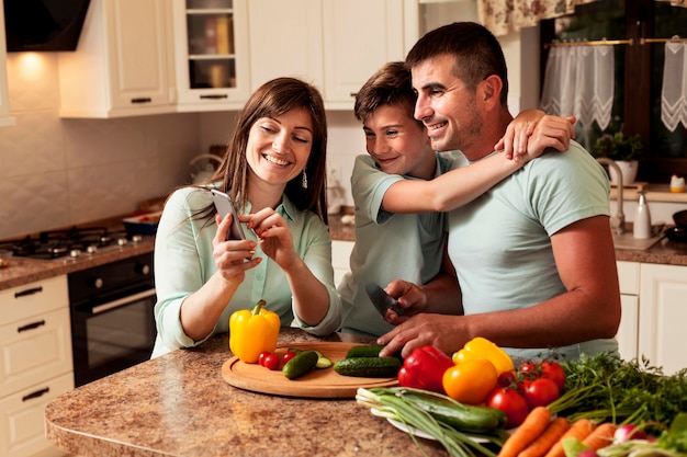 Familie in der Küche, die Bilder auf Smartphone betrachtet