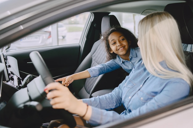 Familie in einem Autosalon. Frau, die das Auto kauft. Kleines afrikanisches Mädchen mit mther.