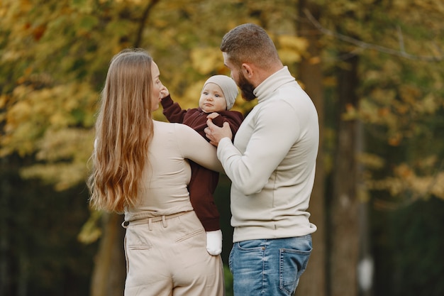 Familie in einem Herbstpark. Mann in einem braunen Pullover. Nettes kleines Mädchen mit den Eltern.