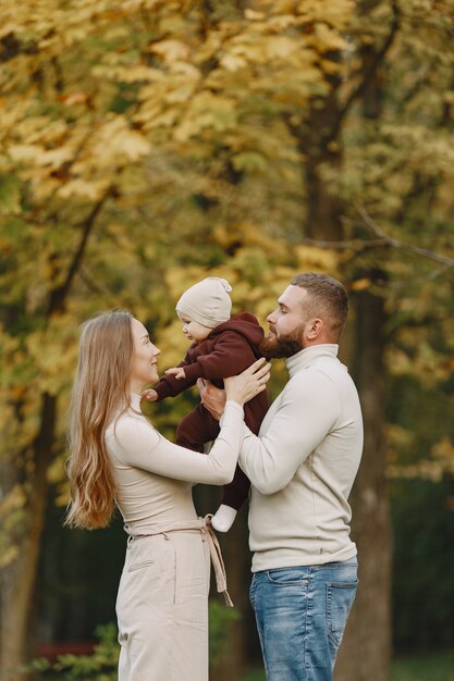 Familie in einem Herbstpark. Mann in einem braunen Pullover. Nettes kleines Mädchen mit den Eltern.