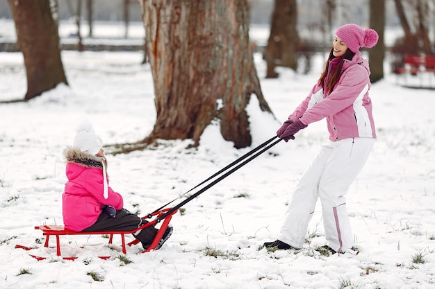 Familie in gestrickten wintermützen auf familienweihnachtsferien. frau und kleines mädchen in einem park. leute, die mit schlitten spielen.