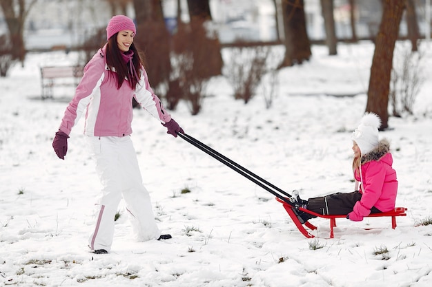 Familie in gestrickten Wintermützen auf Familienweihnachtsferien. Frau und kleines Mädchen in einem Park. Leute, die mit Schlitten spielen.