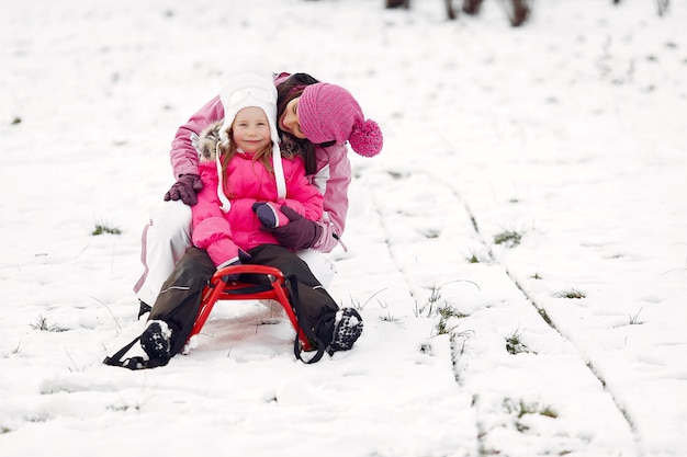 Familie in gestrickten Wintermützen auf Familienweihnachtsferien. Frau und kleines Mädchen in einem Park. Leute, die mit Schlitten spielen.