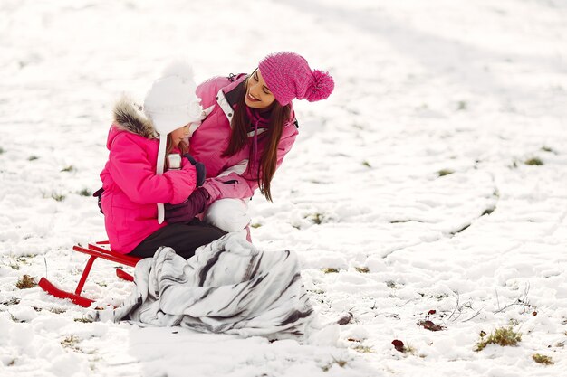 Familie in gestrickten Wintermützen auf Familienweihnachtsferien. Frau und kleines Mädchen in einem Park. Leute mit Thermoskanne.