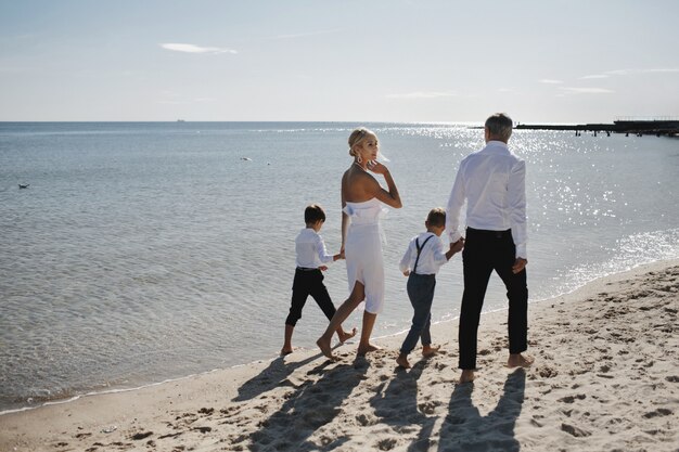 Familie in Luxuskleidung geht an dem warmen, sonnigen Tag barfuß am Sandstrand spazieren