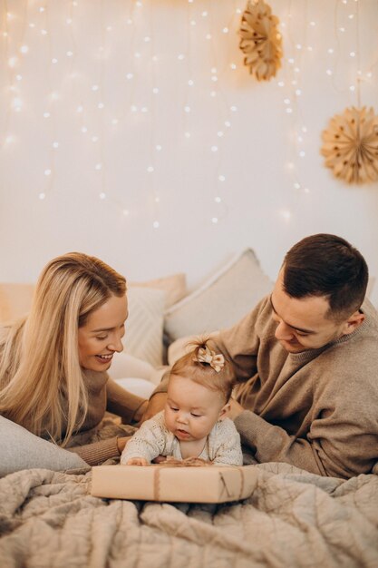 Familie mit Babytochter, die mit Weihnachtsgeschenken auf dem Bett liegt