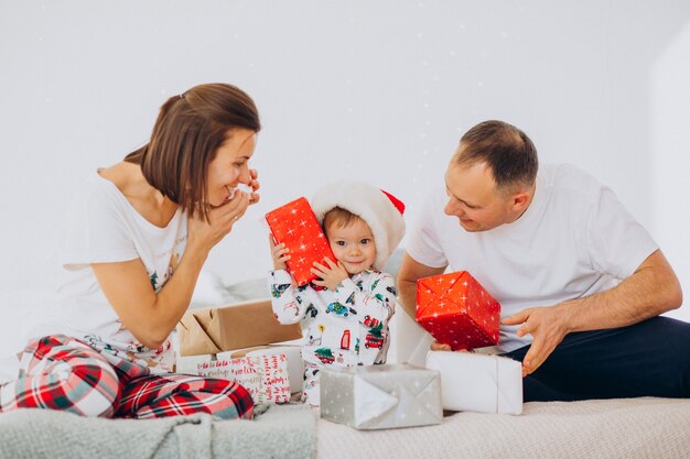 Familie mit kleinem Sohn und Weihnachtsgeschenken, die auf Bett liegen