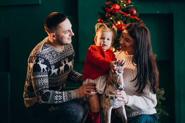 Familie mit kleiner Tochter durch den Weihnachtsbaum, der mit hölzernem Pony spielt