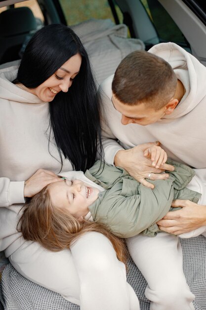 Familie ruht sich nach Tag im Freien aus Vater Mutter ihre Tochter sitzt im Kofferraum Familie trägt beige sportliche Kostüme