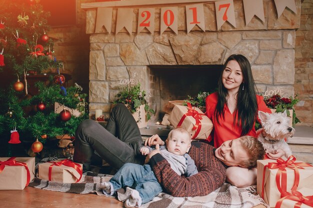 Familie sitzt auf dem Boden mit braunen Geschenken und einem Weihnachtsbaum