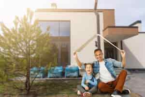 Kostenloses Foto familie sitzt auf rasen im hinterhof, großes modernes haus im hintergrund.